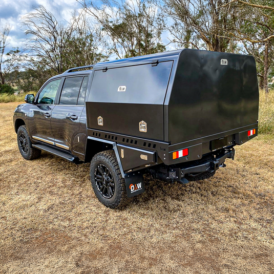 A Nissan Patrol y62 ute conversion fitted with a DMW XT Alloy Tray and fully enclosed canopy, shown parked on dry grassland. The canopy features a sleek matte black finish, secure storage compartments perfect for touring, trade, or recreational use.