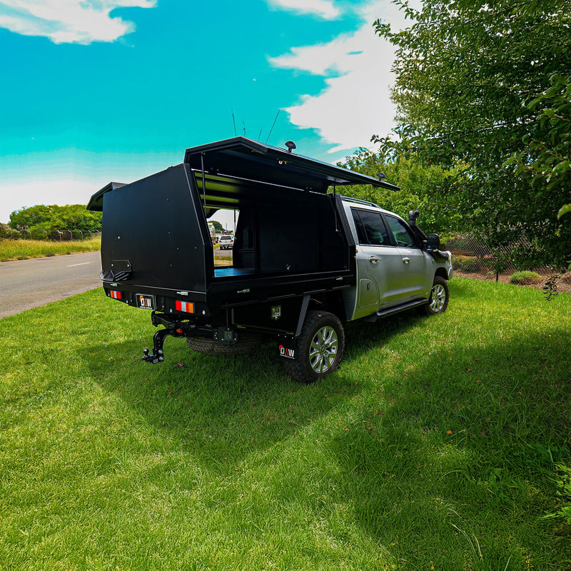Load image into Gallery viewer, A silver dual cab ute equipped with a DMW Deluxe Alloy Tray and black canopy with open gullwing doors, shown parked on a bright green lawn beside a rural road. The spacious canopy is ready for custom fit-outs, offering a blank canvas for touring, camping, or work-ready storage solutions.