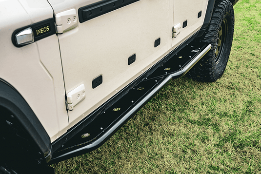 Heavy-duty DMW rock sliders fitted to an INEOS Grenadier, providing reinforced side protection and a practical step platform. Designed for rugged off-road performance with a precision black powder-coated finish and integrated mounting points.