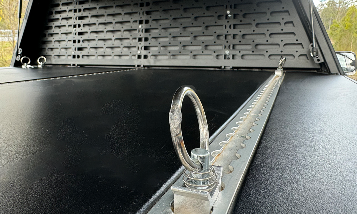 Detailed view of a heavy-duty tie-down ring mounted on an adjustable track system inside a DMW tub replacement canopy. The textured platform and MOLLE panel backdrop provide flexible cargo management options for securely anchoring tools, gear, or camping equipment in a Ford Ranger.