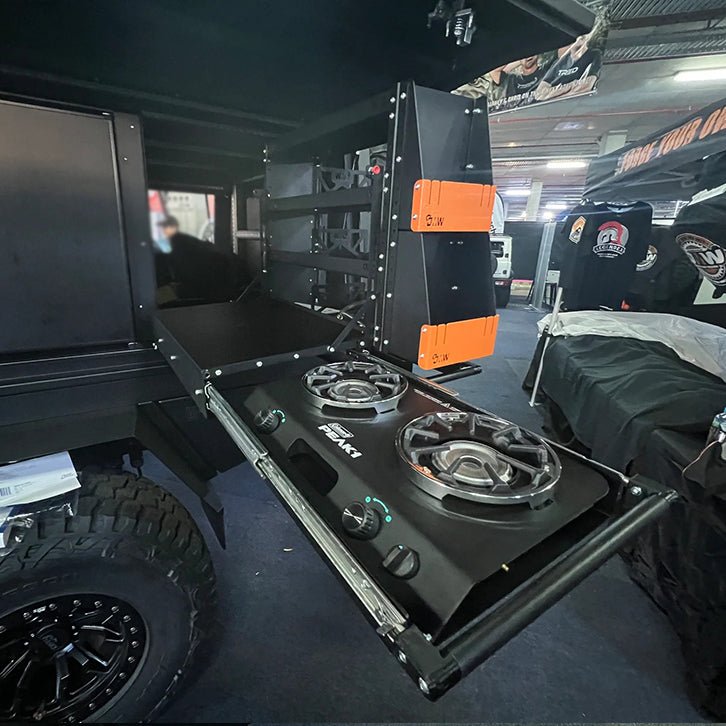 Load image into Gallery viewer, Compact DMW kitchen and pantry system installed in a ute canopy, shopwing a dual-burner gas stove on a slide-out tray and vertically stacked orange-accented storage compartments. Designed for overland cooking and efficient space management in off-road setups.
